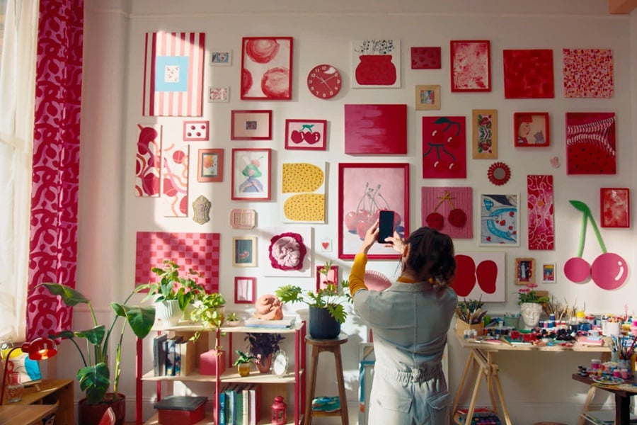 Soggiorno con arte a tema ciliegie appesa con strisce Command, oltre a una mensola con libri e piante e un tavolo con materiale artistico.
